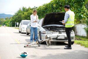 A woman stands next to her broken bike and a car as she wonders how long a bicycle accident claim takes.