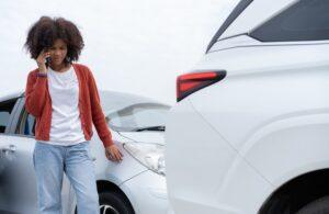 Woman on phone looking at damage after car accident
